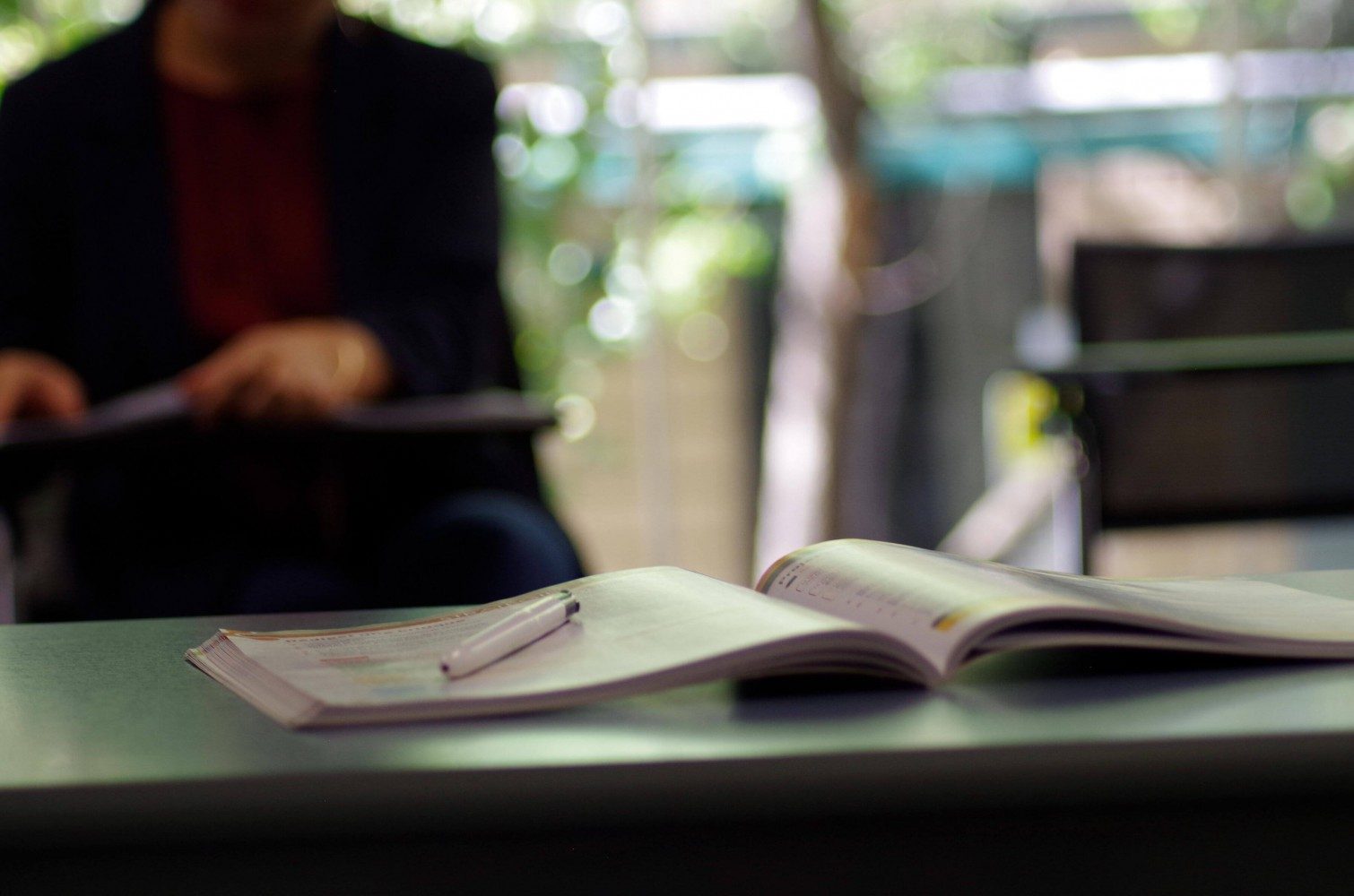 An open textbook with student or teacher in the background 