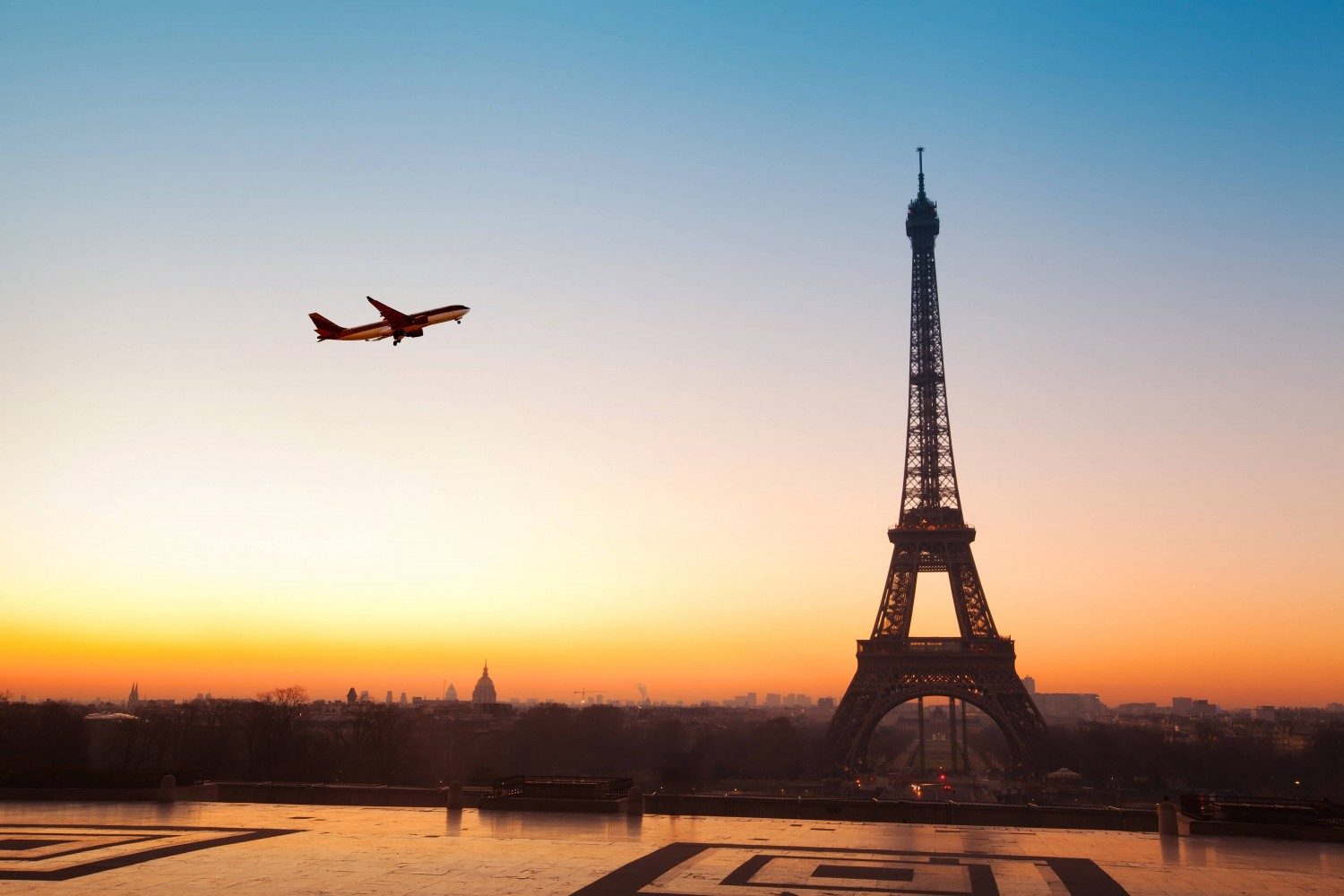 A plane flies in sky in Paris with Eiffel Tower in background